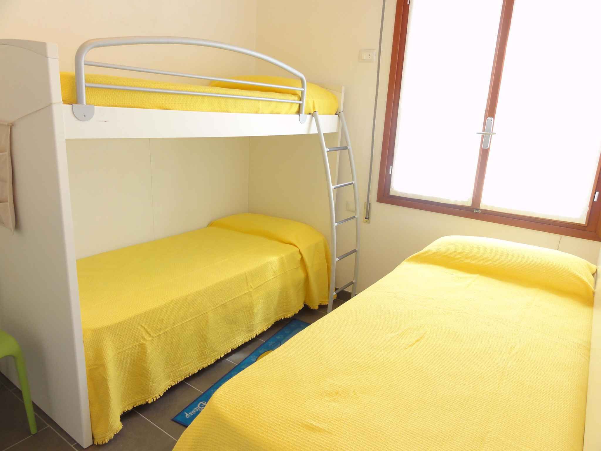 A dormitory room with two beds, a bunk bed, and a window.