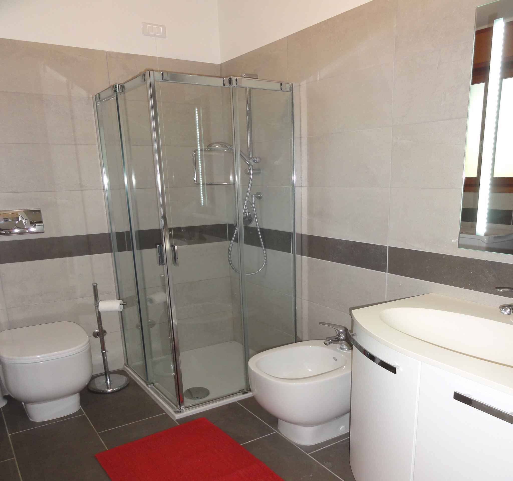 Un baño moderno con ducha envuelta en vidrio, inodoro, bidé y lavamanos con espejo.