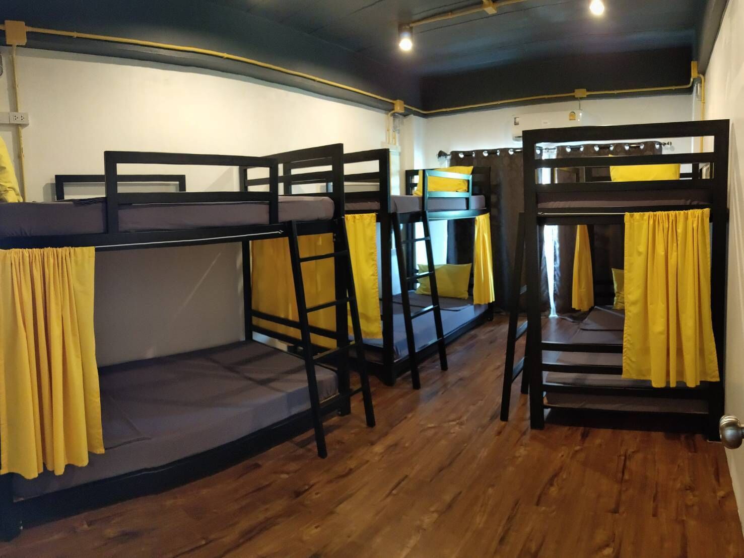 A dormitory room with bunk beds, wooden floors, and yellow curtains.