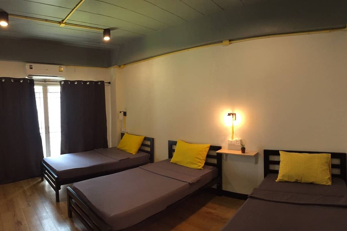 Une chambre avec trois lits simples, chacun étant équipé d’un oreiller et d’une table de chevet avec une lampe.