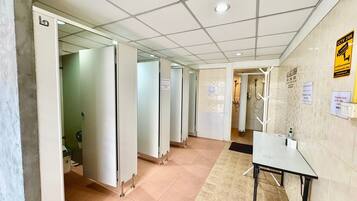 A hotel corridor with multiple doors, a tiled floor, a table with chairs, and a shower area.