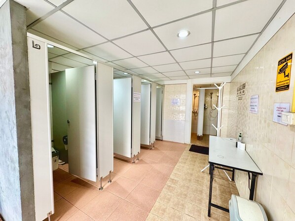 A hotel corridor with multiple doors, a tiled floor, a table with chairs, and a shower area. - Best Bed Suvarnabhumi - Hostel (Bang Phli)
