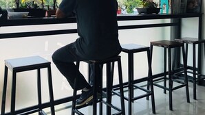 Une personne assise sur un tabouret au bar, avec vue sur des plantes et une fenêtre.