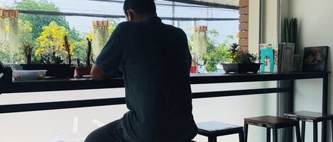 A person seated on a stool at a bar with a view of plants and a window.