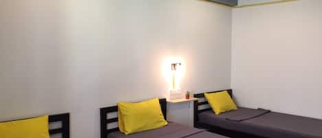 A dormitory room with three single beds, each with a yellow pillow.