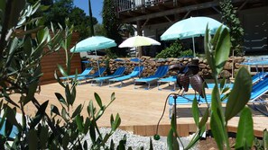 Área de piscina com espreguiçadeiras azuis, guarda-sóis e uma escultura decorativa de pássaro.