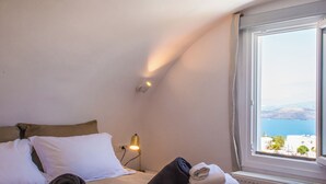 Una cama bien hecha con toallas dobladas, una lámpara y vista al mar a través de una ventana.