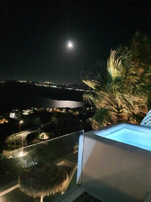 Vista notturna da un balcone con piscina, palme e uno skyline sullo sfondo.