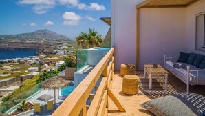 Un balcón con baranda de madera que da a una piscina y una vista panorámica del mar y edificios a la distancia.