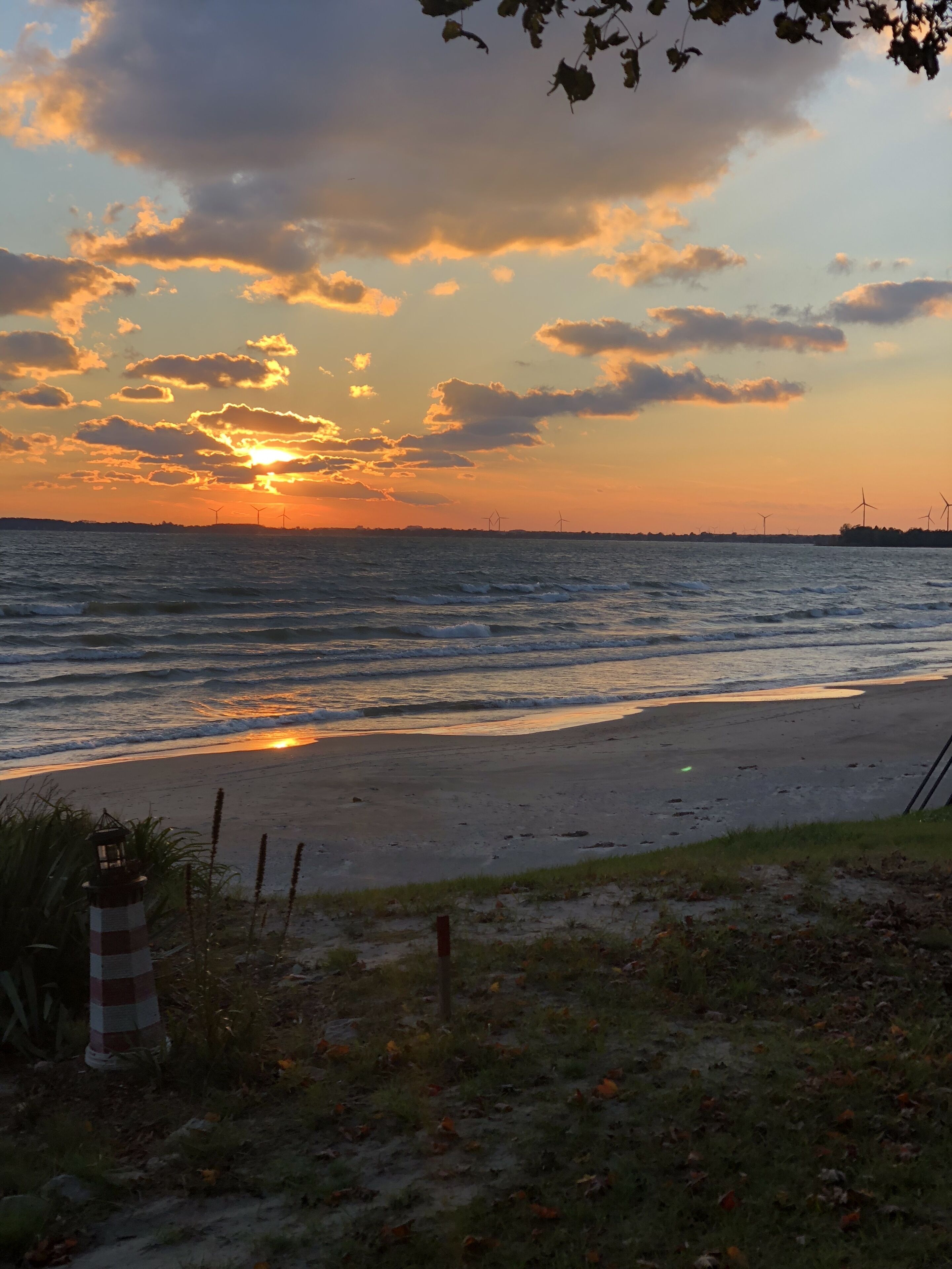 A beach with a lighthouse, ocean waves, and wind turbines in the distance.