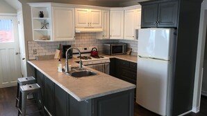 A kitchen with white cabinets, a stainless steel refrigerator, a microwave, a kettle, and a sink.
