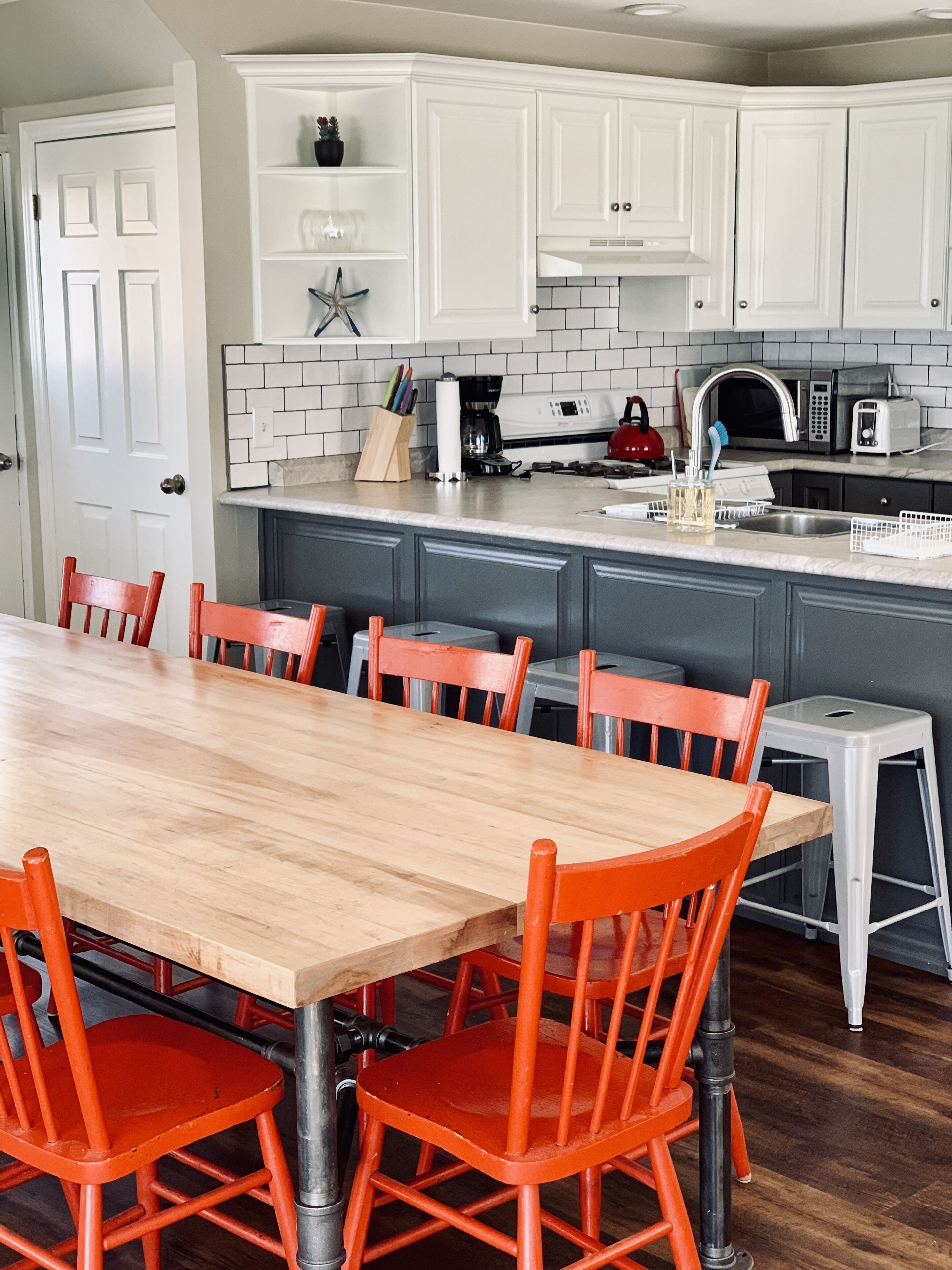 A kitchen with white cabinets, a wooden dining table, and orange chairs.