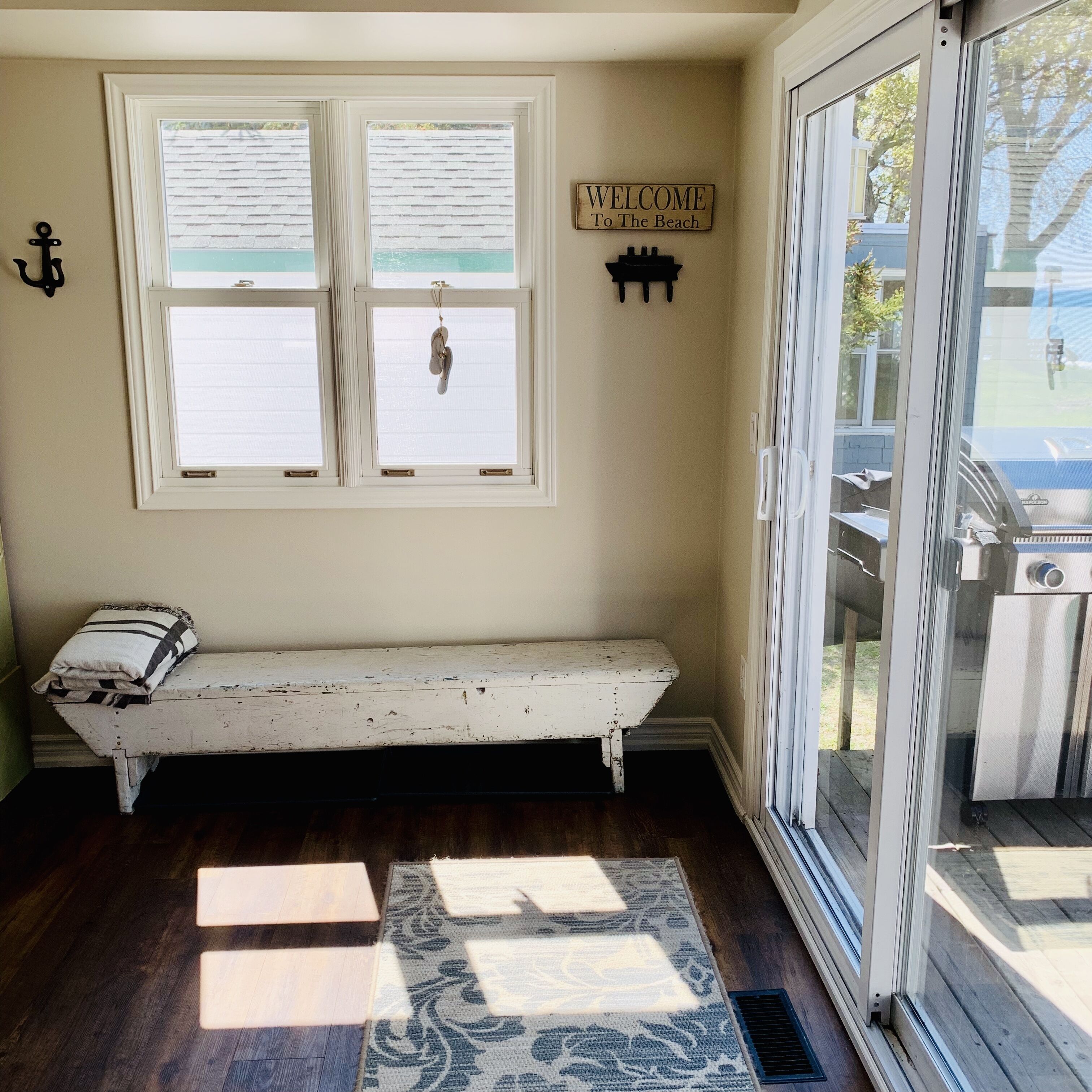 A room with a bench, a 'Welcome To The Beach' sign, and a view of the beach through a large window.