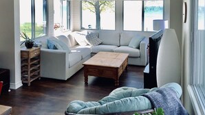A spacious living room with a large sectional sofa, a wooden coffee table, and a view of the outdoors through large windows.
