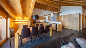 Eine moderne Küche mit Holzschränken, ein Essbereich mit Tisch und Stühlen sowie eine Couch im Vordergrund.