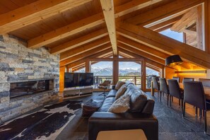 A cozy living area with a stone fireplace, leather sofa, and a dining area with chairs. - Montagnard 12 - Spa Access (Haute-Nendaz)