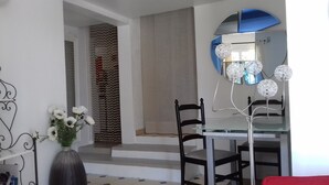 A dining area with a glass table, two chairs, a vase with flowers, and a decorative mirror with a blue accent.