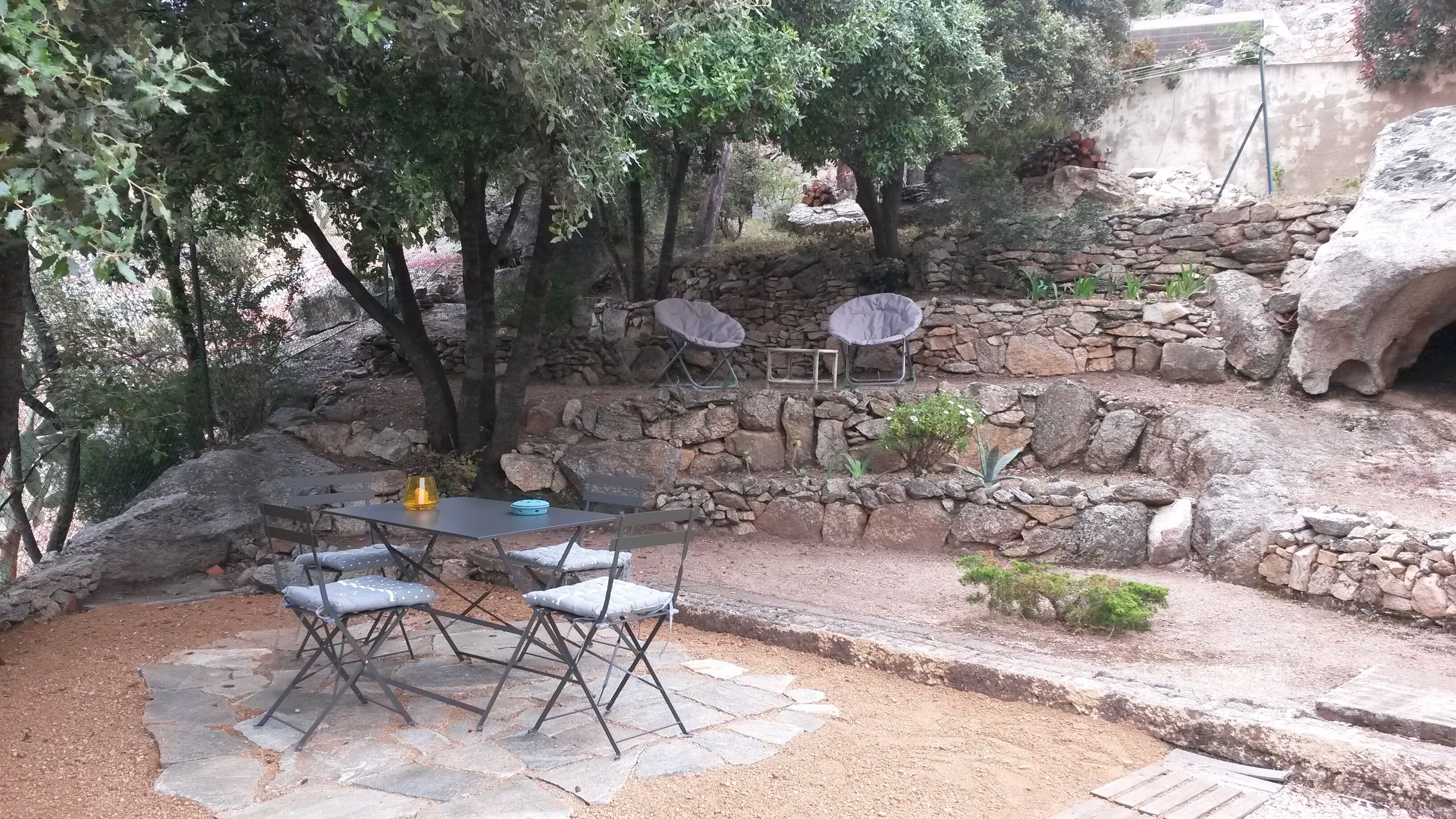 An outdoor patio with stone flooring, a table with chairs, and a stone wall with a fire pit.