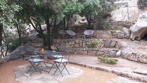 An outdoor patio with stone flooring, a table with chairs, and a stone wall with a fire pit.