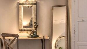 A room with a wooden chair, a small table, and two mirrors with decorative frames.