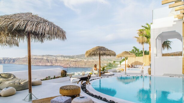 A pool area with a view of the sea, lounge chairs, and a thatched umbrella.