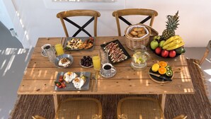 A wooden dining table with various breakfast items, including fruits, pastries, and beverages.