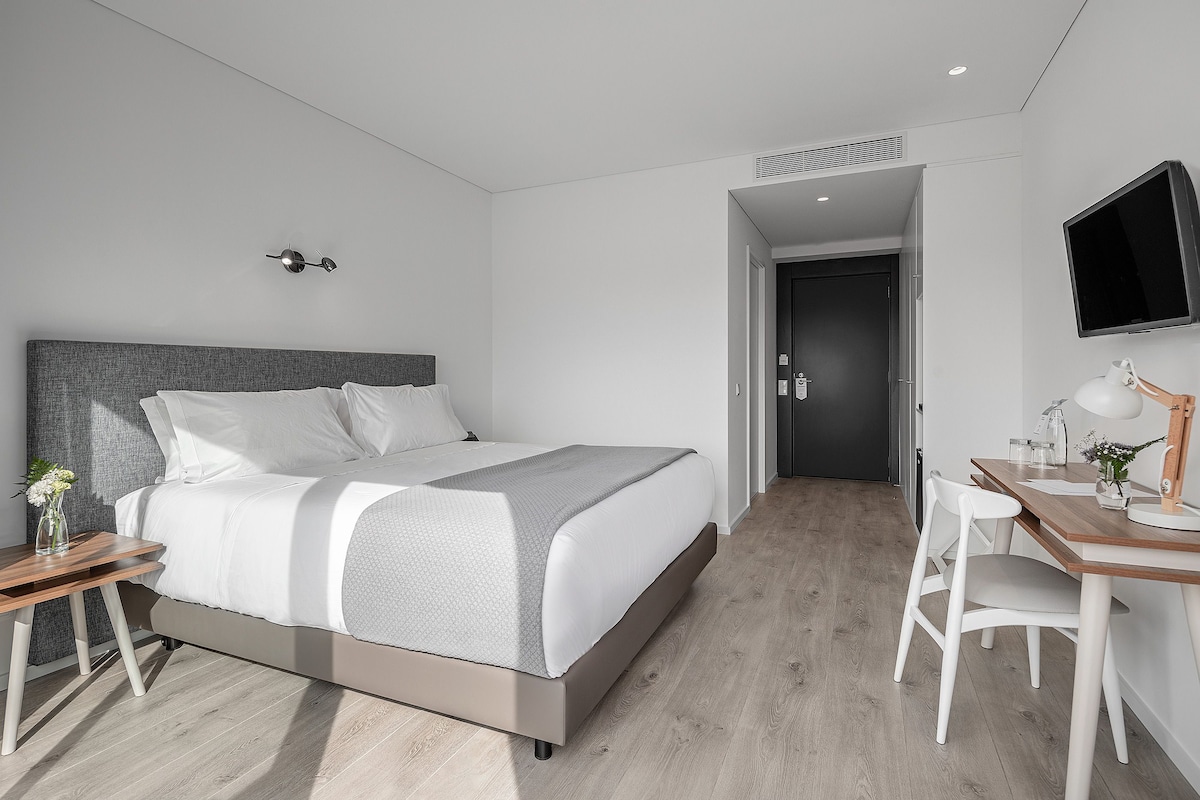 Una habitación de hotel moderna con cama, mesita de noche, escritorio, silla y televisor montado en la pared.