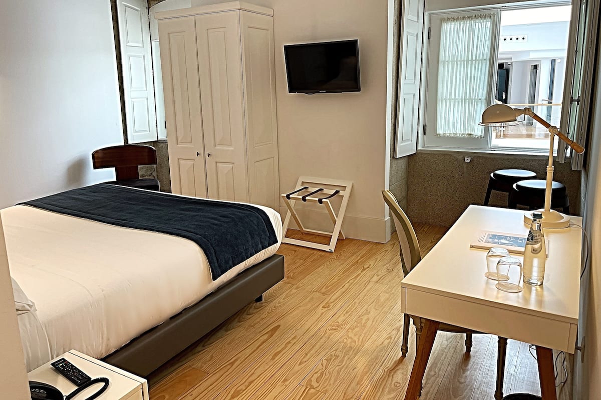 Quarto de hotel com cama, escrivaninha, cadeira, televisão e guarda-roupa.