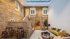 A spacious interior with a stone wall, a staircase, a yellow sofa, and a bar area with stools. - Caléway Hotel (Vila Nova de Gaia)