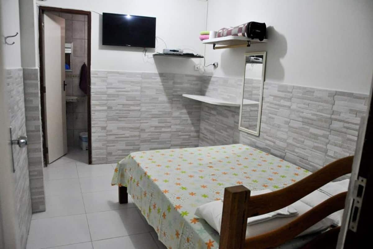 Une chambre à coucher avec un lit, un téléviseur fixé au mur et un miroir au-dessus du lit.