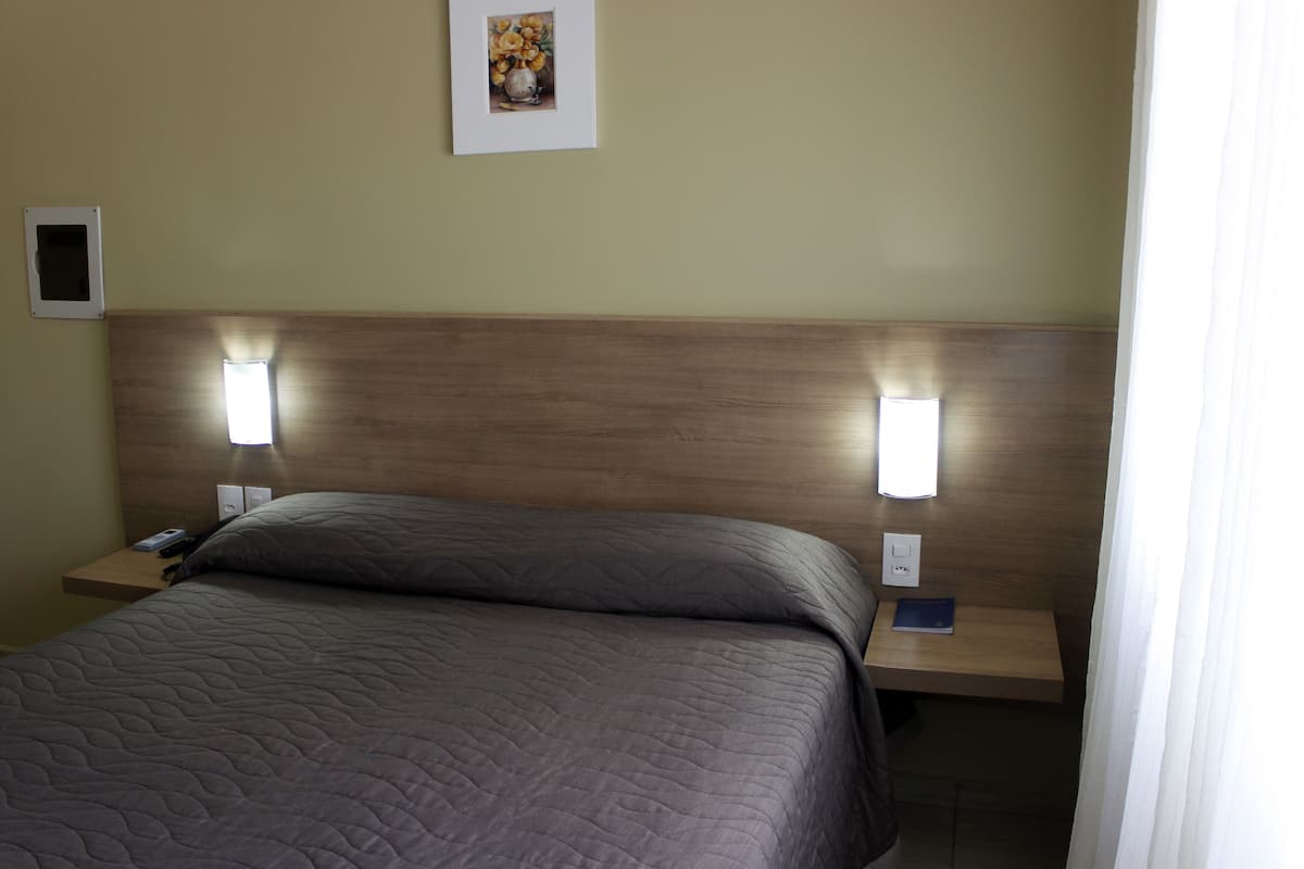 Una habitación de hotel con cama, mesitas de noche, lámpara de pared e imagen enmarcada.