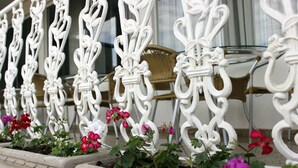 Una cerca de hierro forjado blanco con diseños intrincados, bordeada por macetas con flores rosas y blancas.