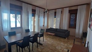 Een kamer met een eettafel, stoelen, een bank en een klein bijzettafeltje.