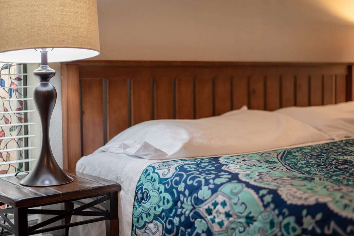 A neatly made bed with a patterned bedspread, a wooden headboard, and a lamp on a bedside table.