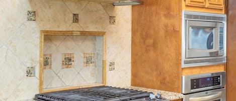 Una cocina con estufa a gas, microondas, horno y salpicadero de azulejos.