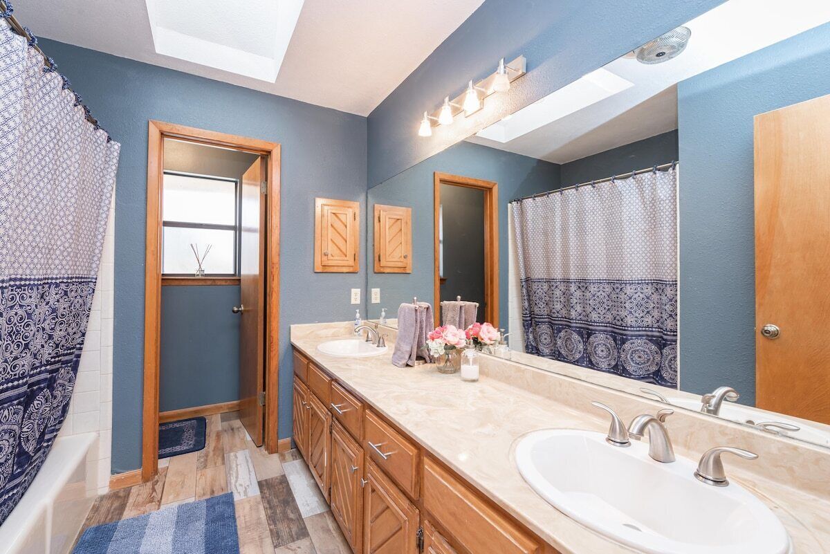 Une salle de bain avec deux lavabos, des meubles en bois, un grand miroir et des rideaux à motifs.