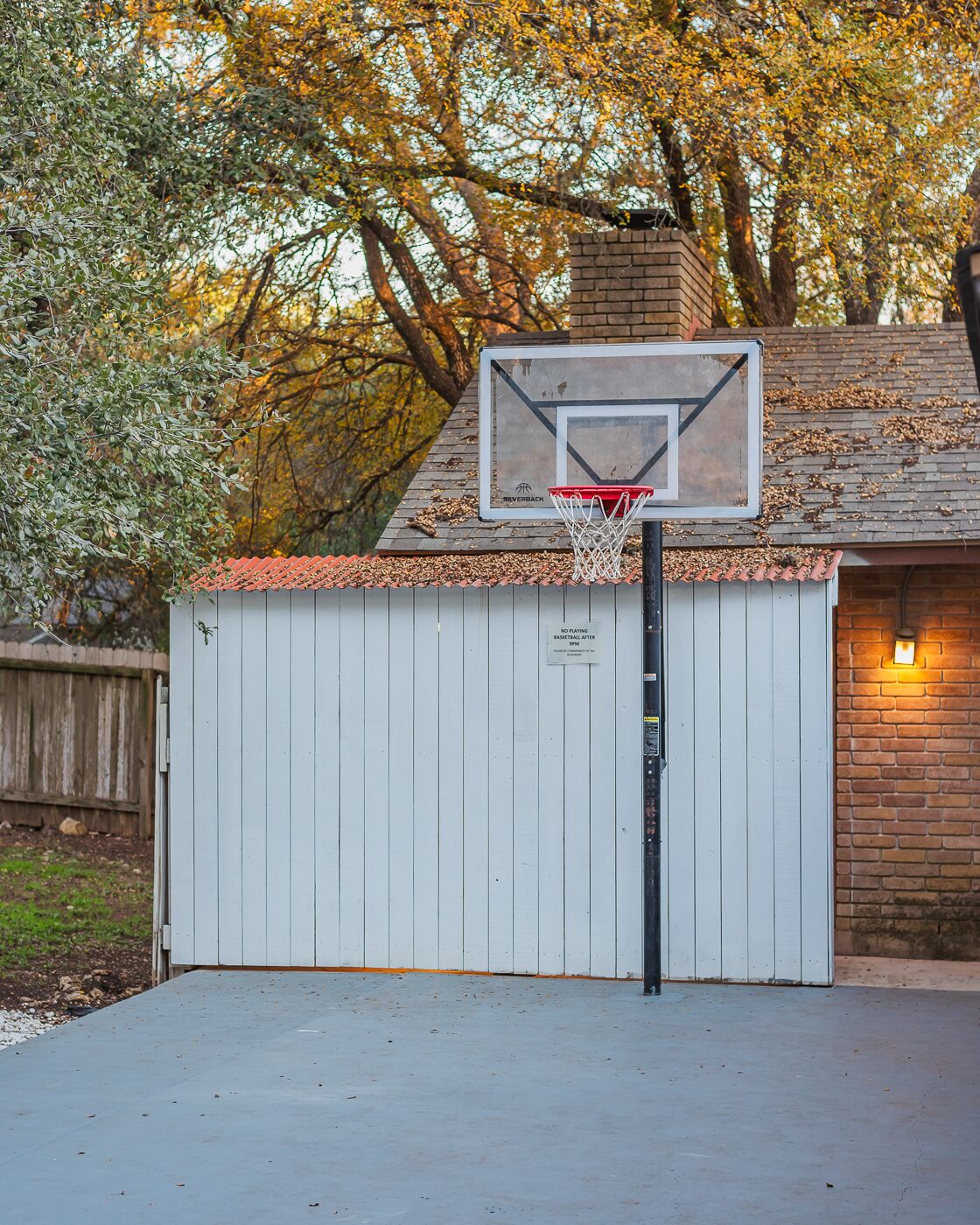 Un aro de baloncesto sobre una puerta de garaje blanca, con una chimenea de ladrillo al fondo.