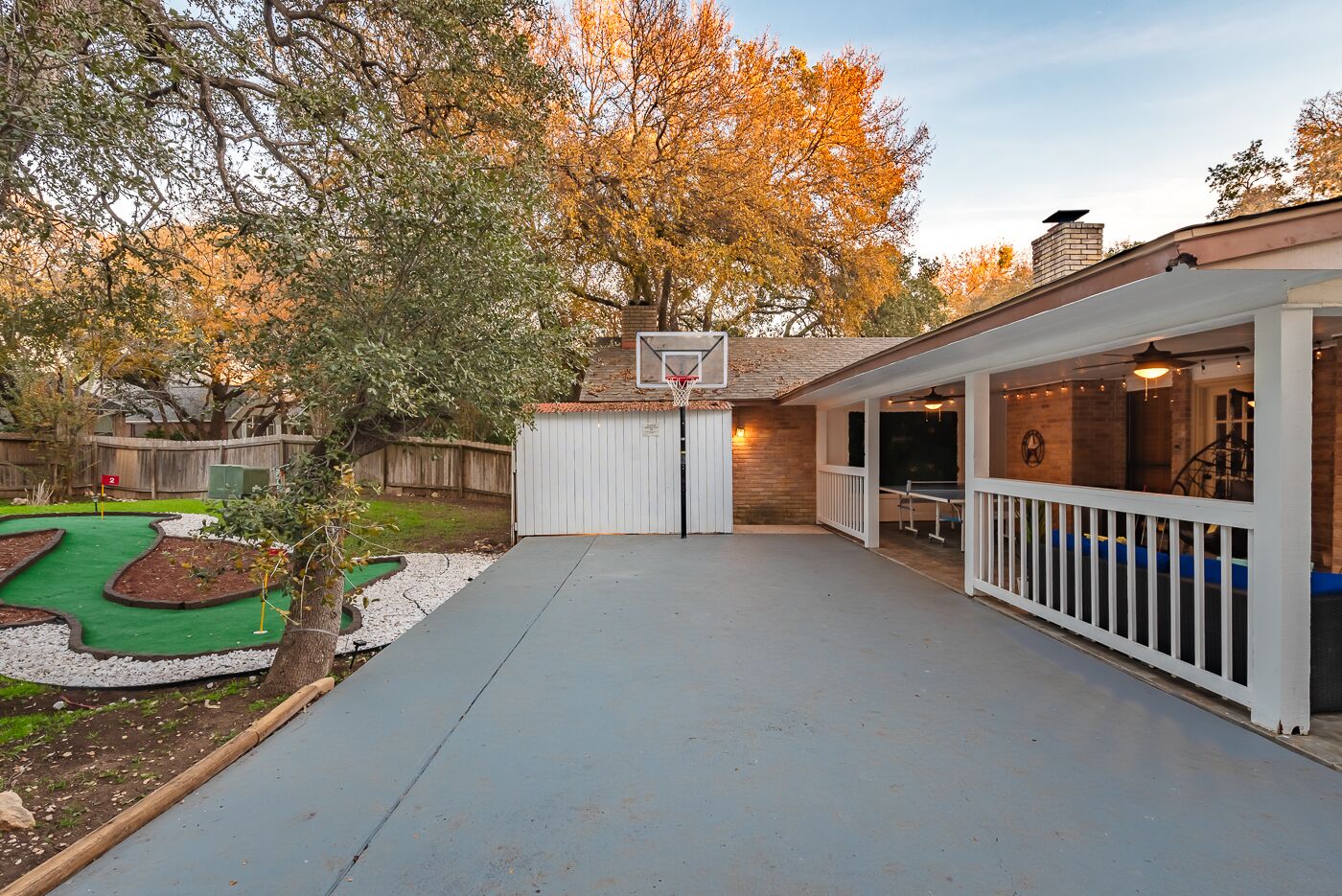 A backyard with a basketball hoop, a ping pong table, and a covered seating area.