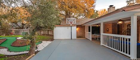 A backyard with a basketball hoop, a ping pong table, and a covered seating area.