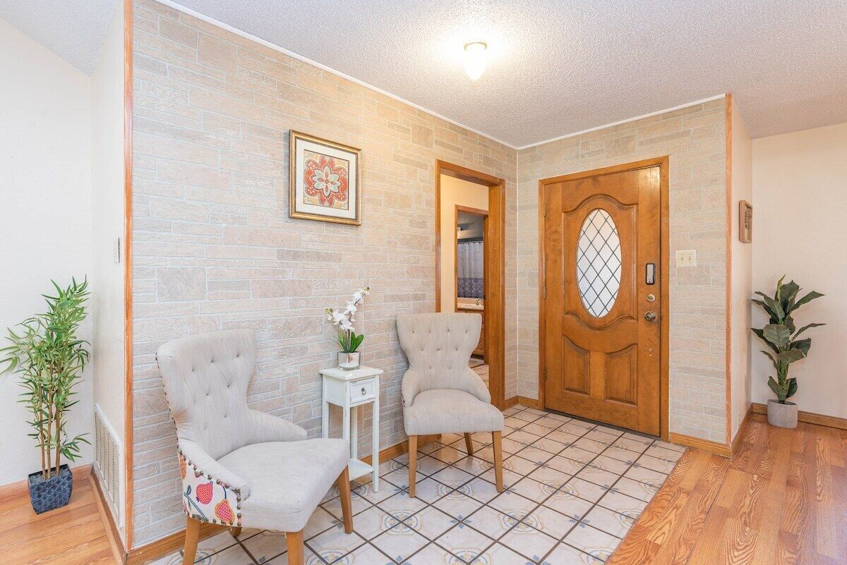 Un pasillo con dos sillones, una mesita con una planta, una puerta de madera y una pared de ladrillo con un cuadro enmarcado.