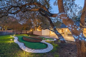 Un parcours de mini-golf avec une zone d’putting verdoyante, des petits galets blancs disposés sur les bords et une clôture en bois en arrière-plan.