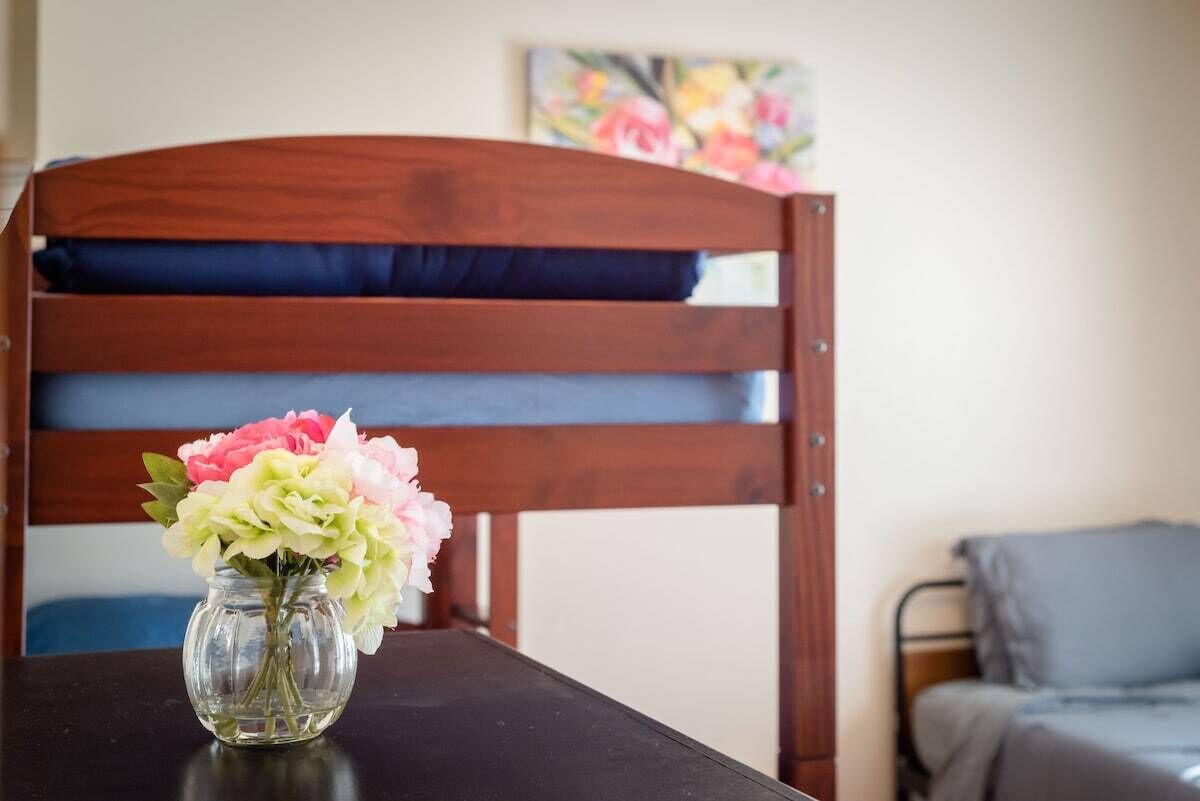 Una silla de madera con un cojín oscuro, un jarrón con flores y un cuadro en la pared.