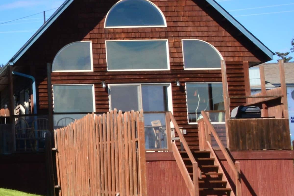 A wooden building with large arched windows and a wooden staircase leading to a deck.