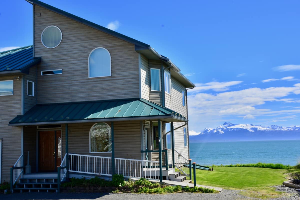 A two-story house with a porch, a wooden door, and a view of a lake and mountains.