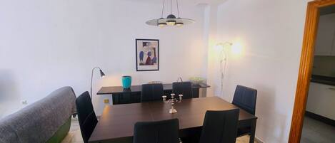 A dining area with a rectangular table, black chairs, a blue vase, a framed picture, and a pendant light.