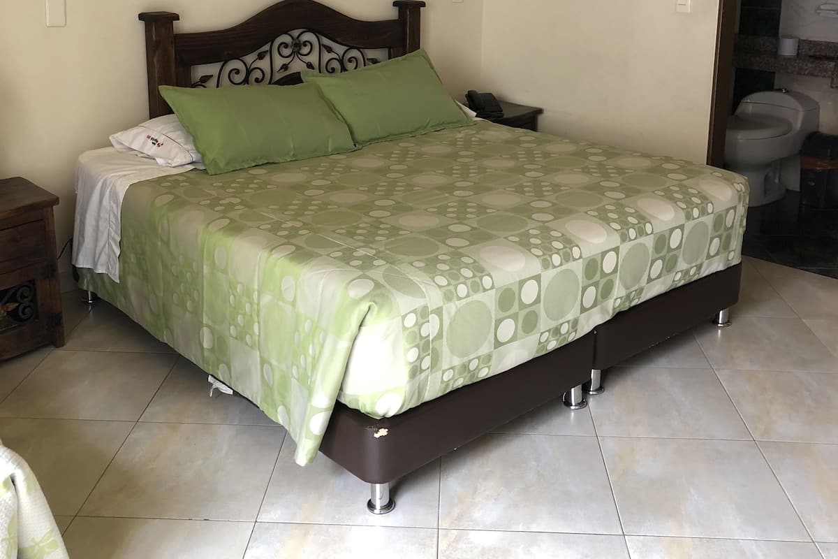 Un dormitorio con cama, mesita de noche, teléfono en la pared y un baño visible a través de una puerta abierta.