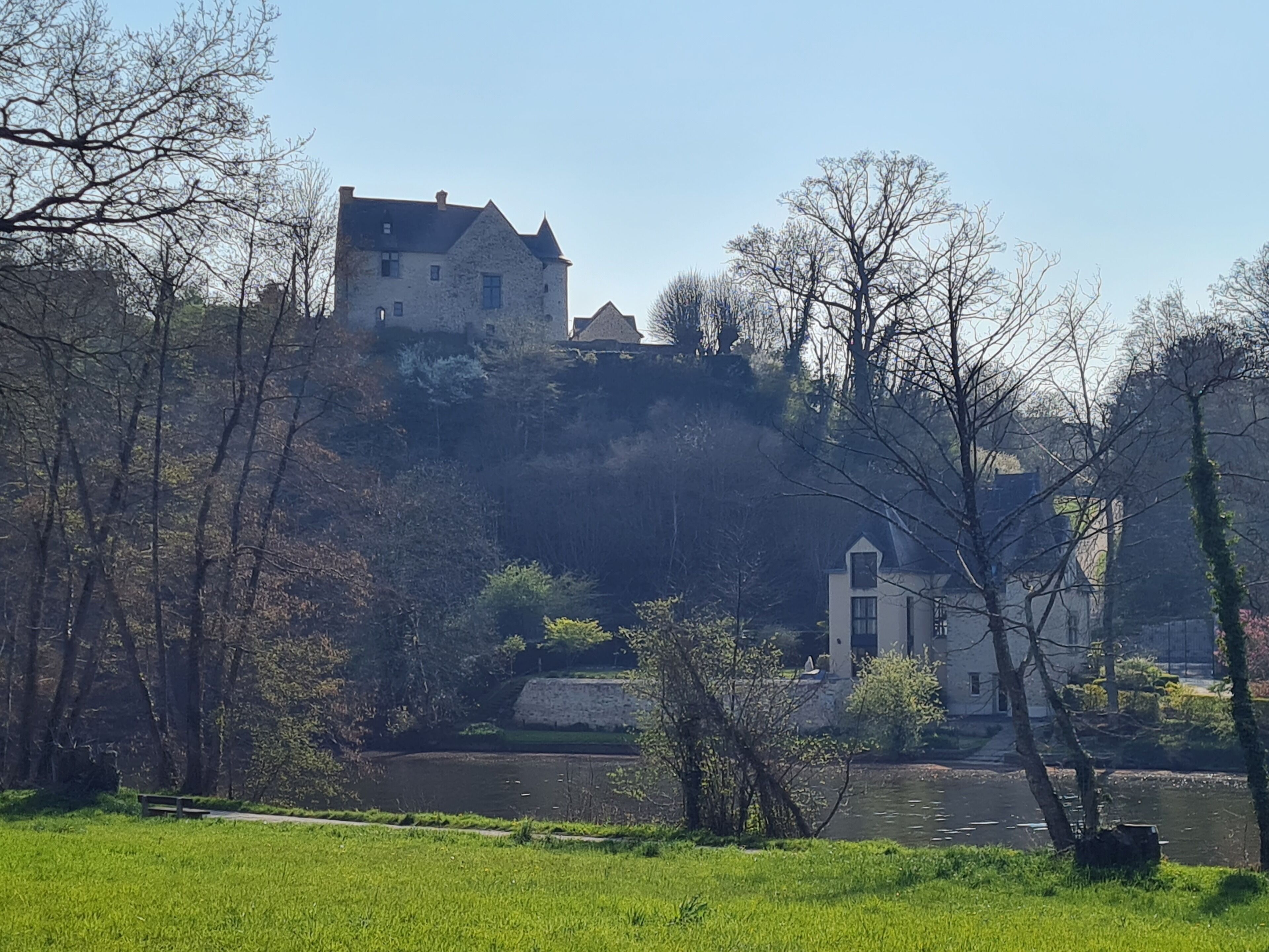 Un bâtiment qui ressemble à un château, avec une façade en pierre, situé sur une colline surplombant une rivière.