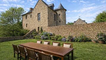 A stone building with a tower, surrounded by a stone wall and a grassy area with a wooden table and chairs.