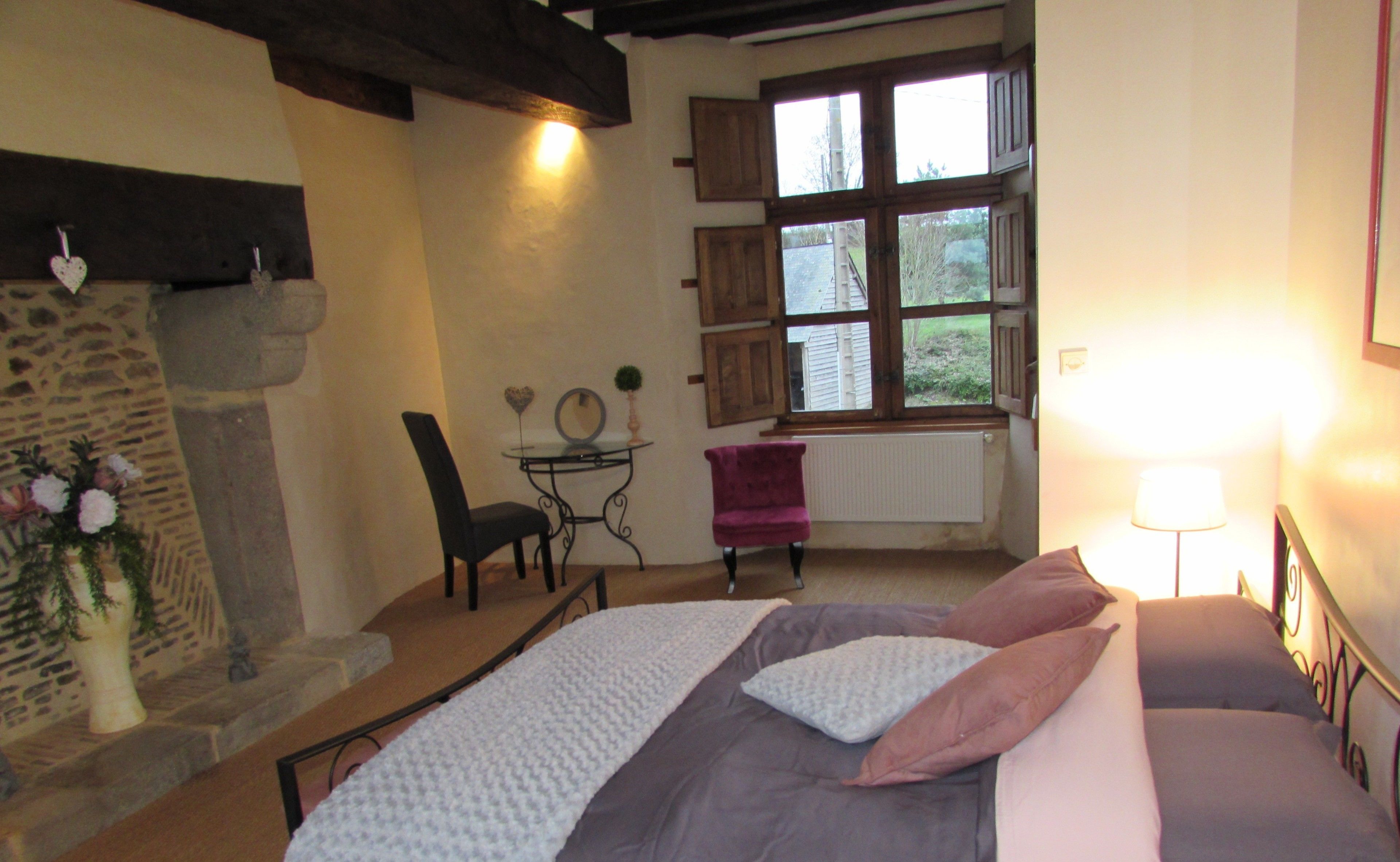 Un dormitorio con cama, una silla, una mesita, un espejo y una ventana.