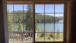 A room with a large window offering a view of a lake surrounded by trees. - Alexander lake lodge (Cedaredge)